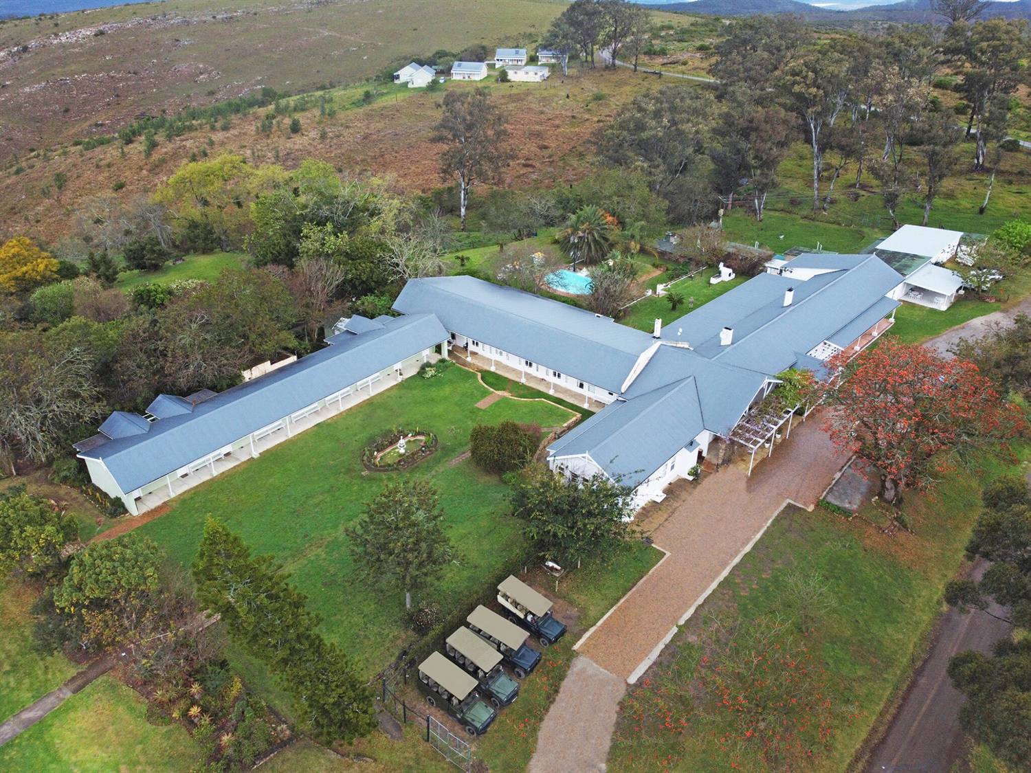 Aerial view of the hotel's long white buildings and lawns set among trees on the mountain top