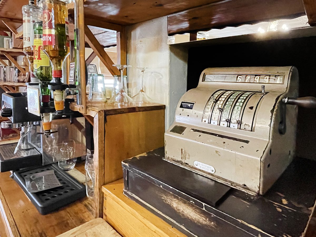 A hand-cranked brass and enamel cash register on the bar counter