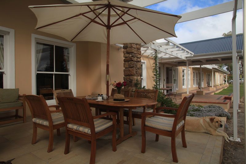 A patio dining table under an umbrella at dusk with a dog resting alongside