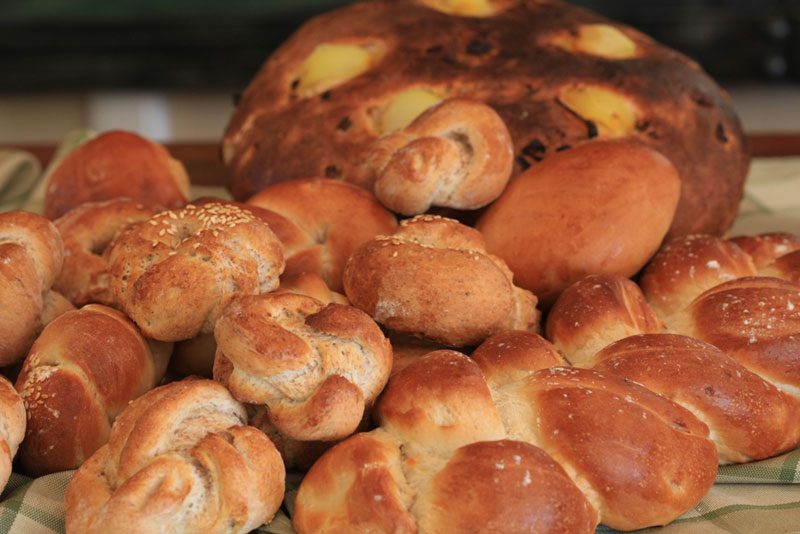 A basket of freshly baked bread rolls beside a large crusty loaf