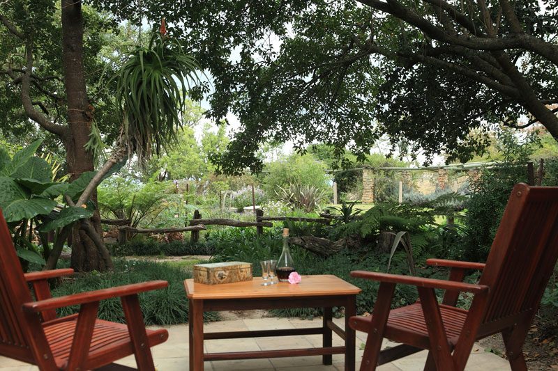 Two wooden chairs and a small table in a shaded corner of the garden