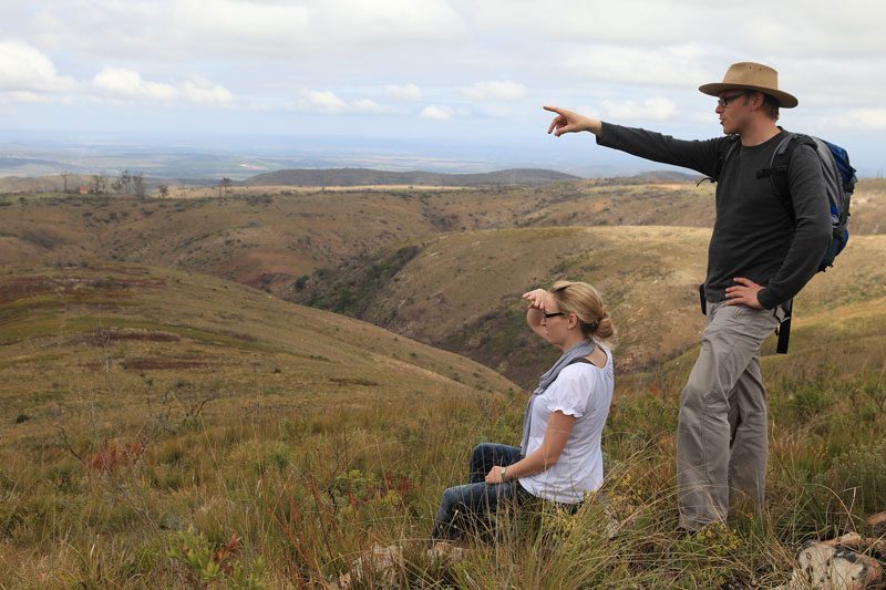 Two hikers pausing on the trail to look out across a wide grassy valley