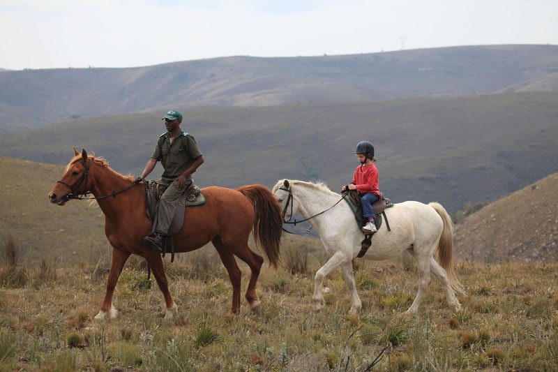 A guide and a young rider on horseback crossing the open grassland hills