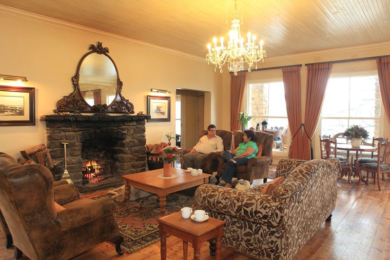 Two guests sitting and talking beside the lit stone fireplace under an ornate mirror