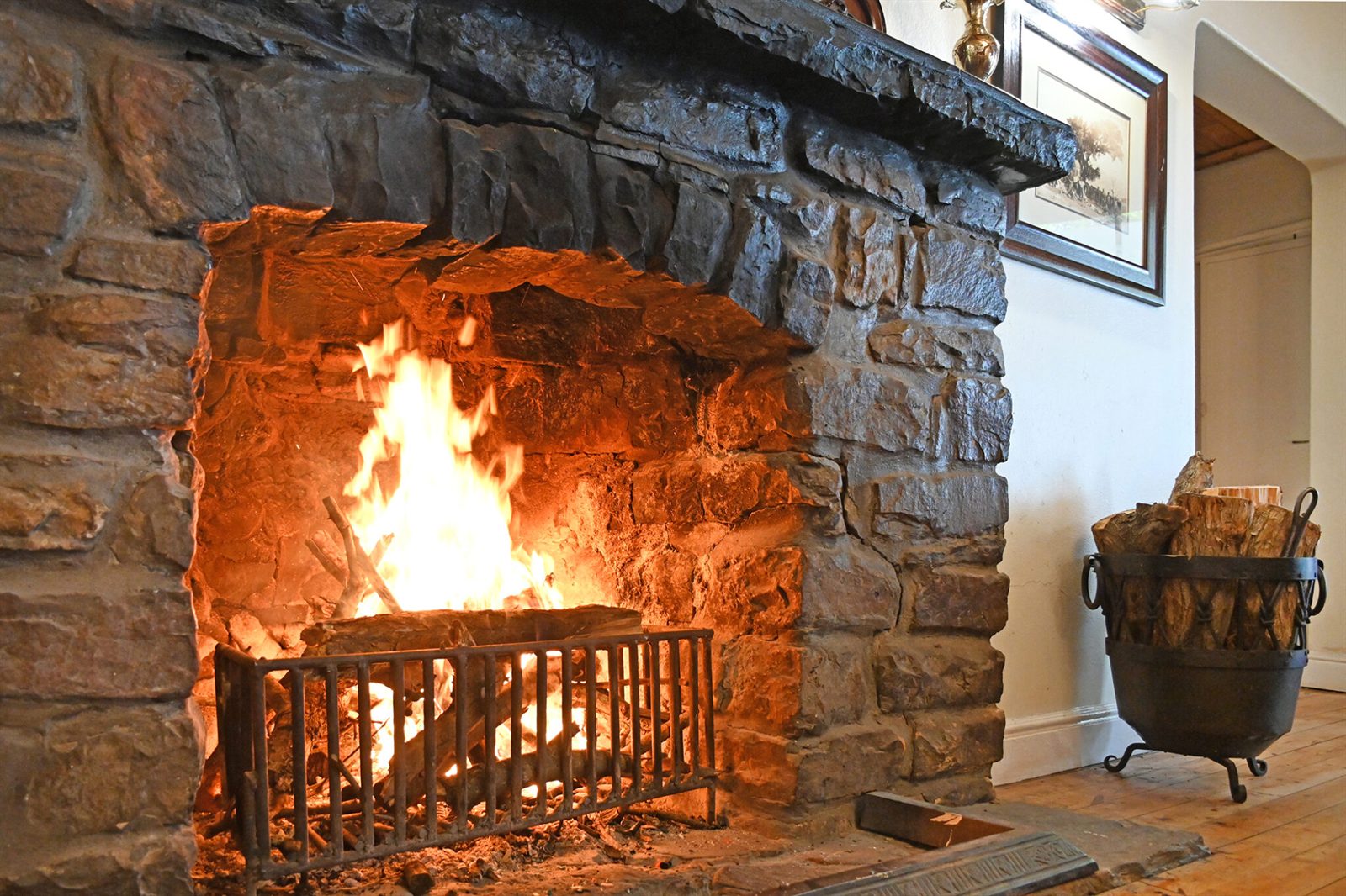 A log fire burning in the lounge's deep stone fireplace, with a basket of firewood alongside