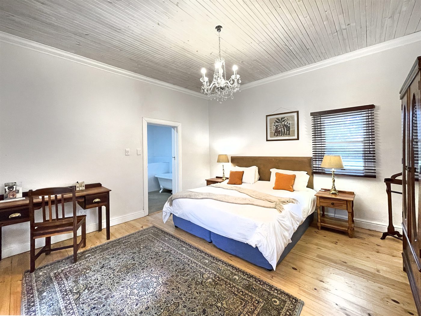 A Manor bedroom with a chandelier, pressed-pine ceiling, wooden floors and a bathroom beyond