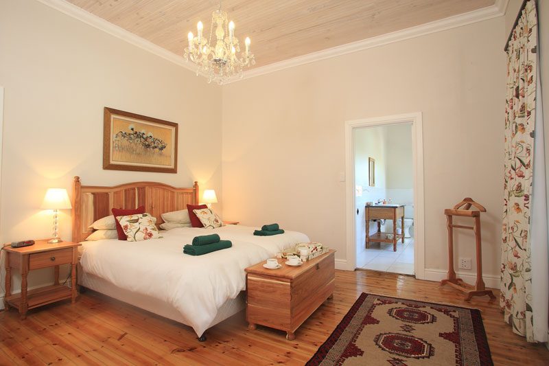 A Manor bedroom with a carved wooden headboard, chandelier and open door to the en-suite bathroom