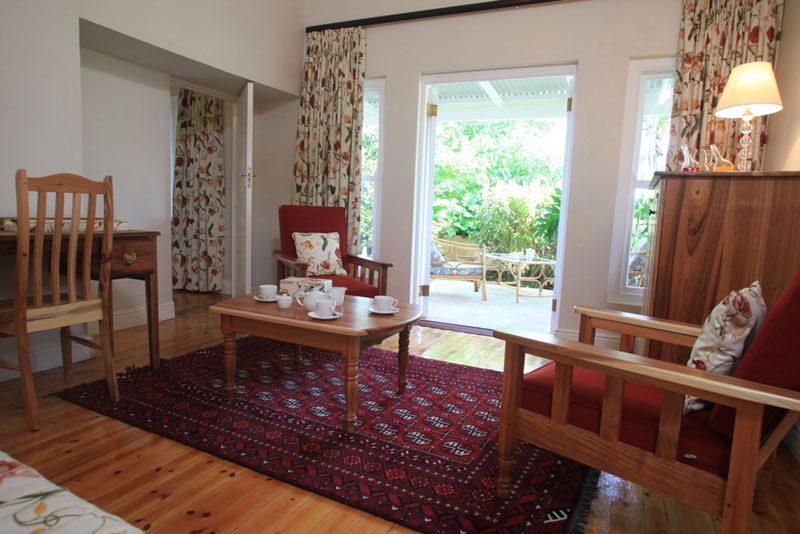 A suite sitting room with a red armchair and a table, patio doors standing open