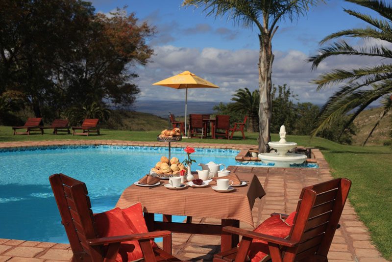 The hotel swimming pool with loungers, a fountain and a table laid for tea, hills beyond