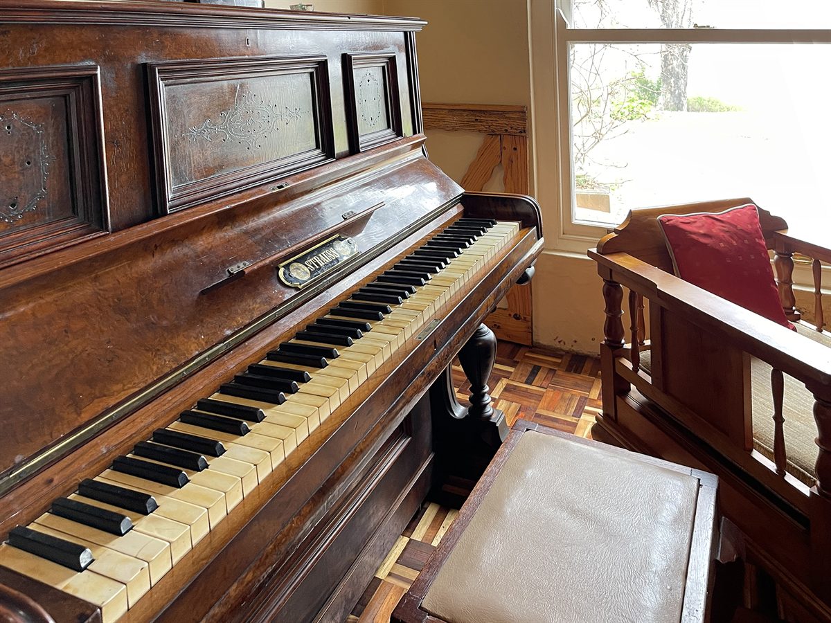 An antique Strauss upright piano with a bronze elephant on its lid, beside a parquet floor