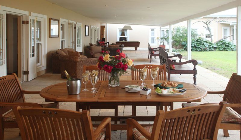 A long covered veranda with wicker lounge seating and a table laid with flowers