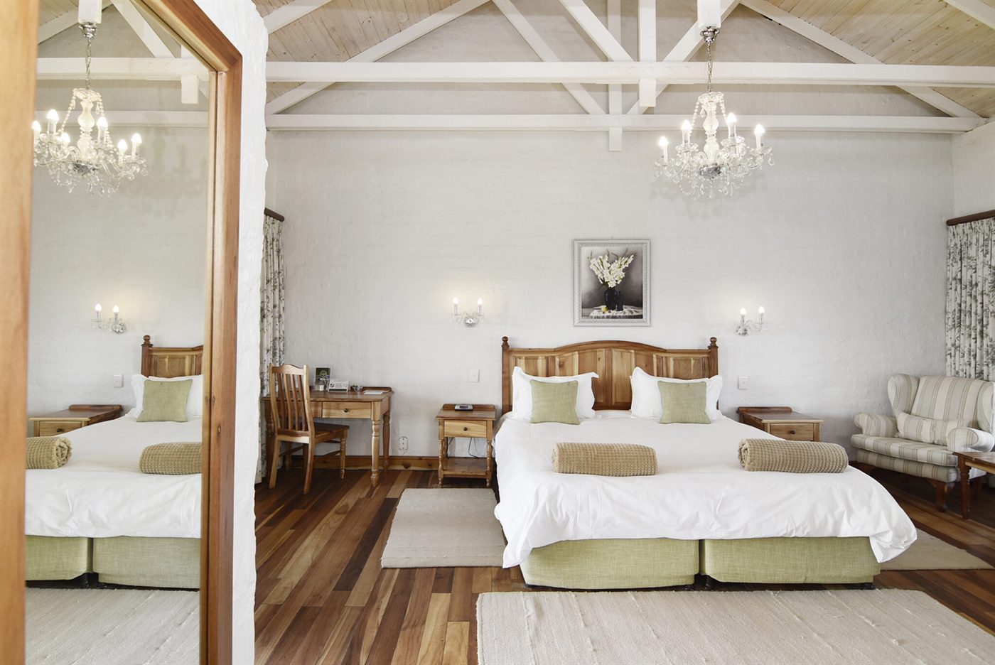 A Village cottage bedroom with white beamed ceiling, chandeliers and dark wood floors