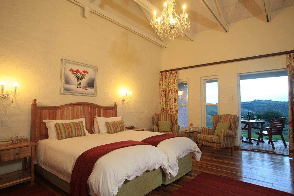 A Village cottage bedroom with beamed ceiling and doors open to a patio with a hillside view