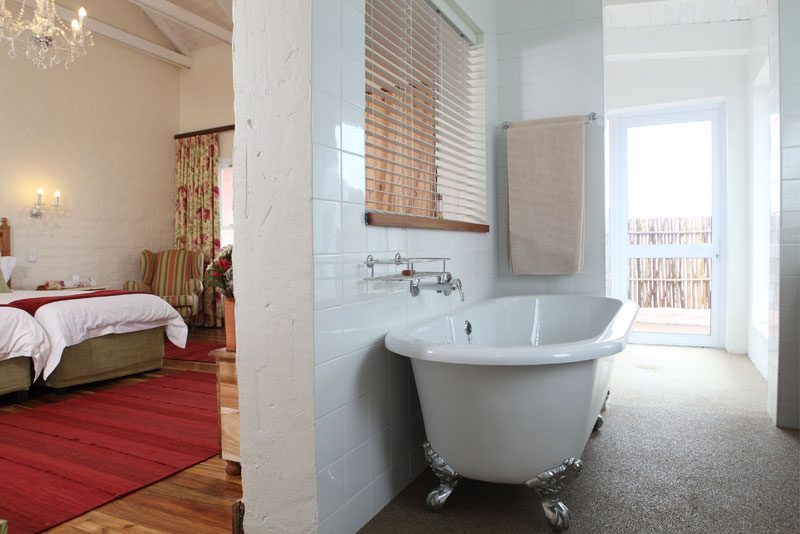 A freestanding claw-foot bath in a cottage en-suite, the bedroom visible beyond