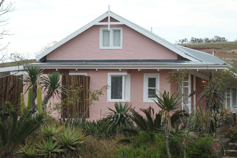 A pink gabled Village cottage behind a garden of aloes and succulents
