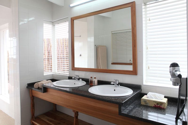 A cottage bathroom with two basins set in a wooden vanity beneath a large mirror