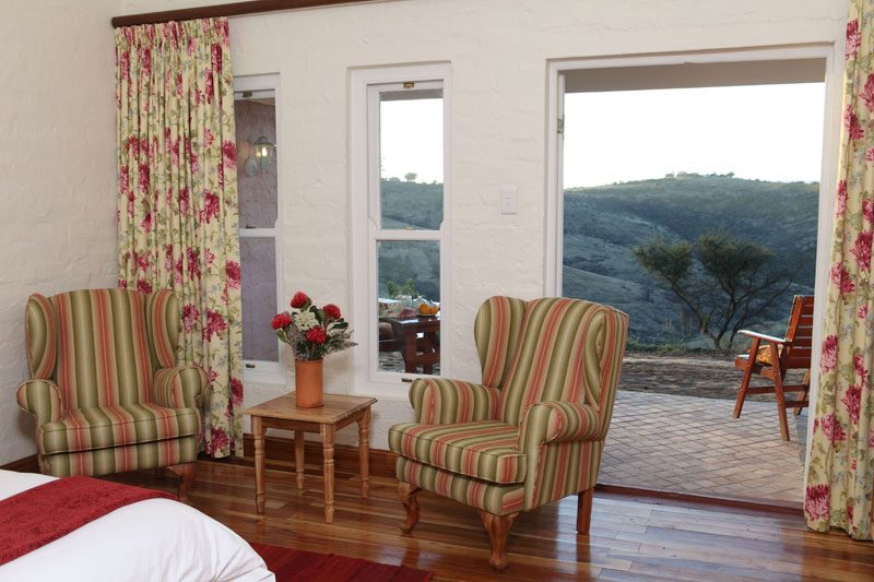 A bedroom seating nook with striped wing chairs and doors onto the patio and hills